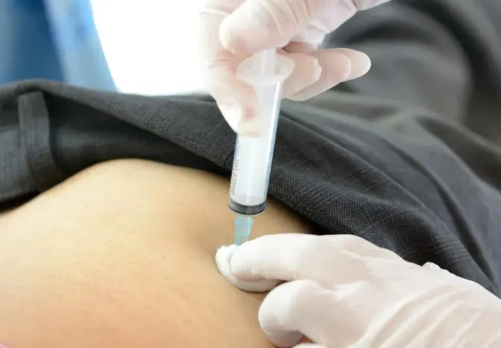 Ręka w białej rękawiczce podaje zastrzyk. Wstrzyknięcie leku aglan 15.