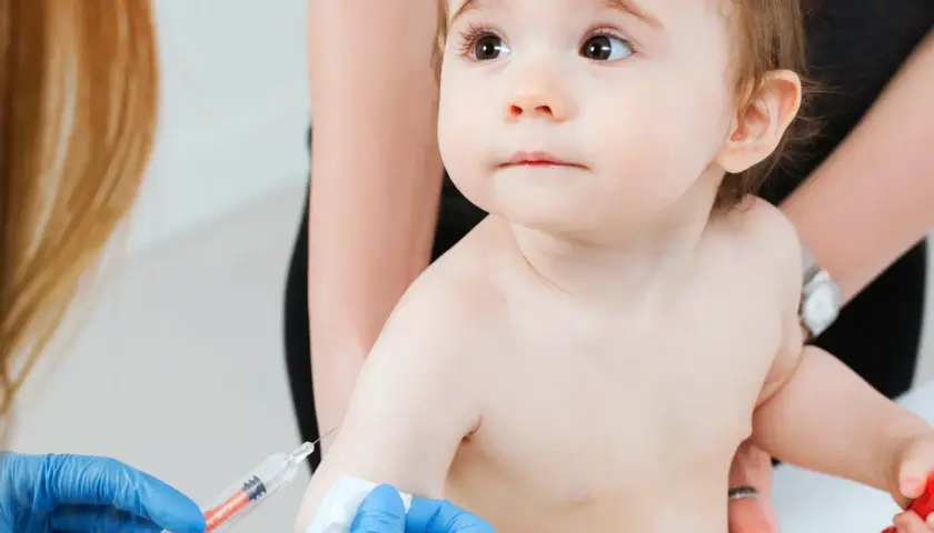 Małe dziecko otrzymuje szczepienie RSV. Ręka w niebieskiej rękawiczce trzyma strzykawkę, gotową do podania leku.