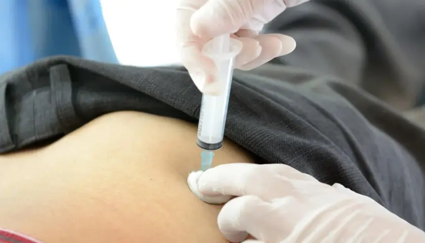 Ręka w białej rękawiczce podaje zastrzyk. Wstrzyknięcie leku aglan 15.