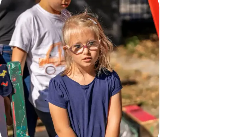 Dziewczynka z zespołem Downa w okularach patrzy w obiektyw. Obok stoi chłopiec.