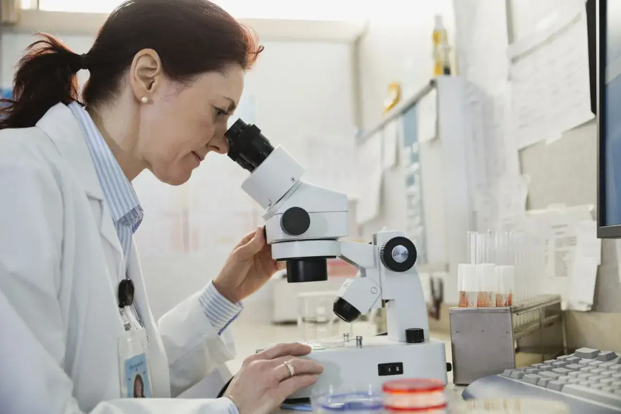 Naukowczyni prowadzi badanie histopatologiczne pod mikroskopem, analizując próbki w laboratorium.